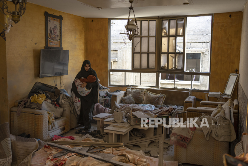 Seorang wanita Palestina menggendong anak diantara reruntuhan bangunan rumahnya yang hancur akibat serangan Israel di Rafah, Jalur Gaza, Sabtu (9/12/2023). Serangan udara Israel yang membombardir wilayah Rafah mengakibatkan korban jiwa dan lingkungan rumah warga Palestina hancur.
