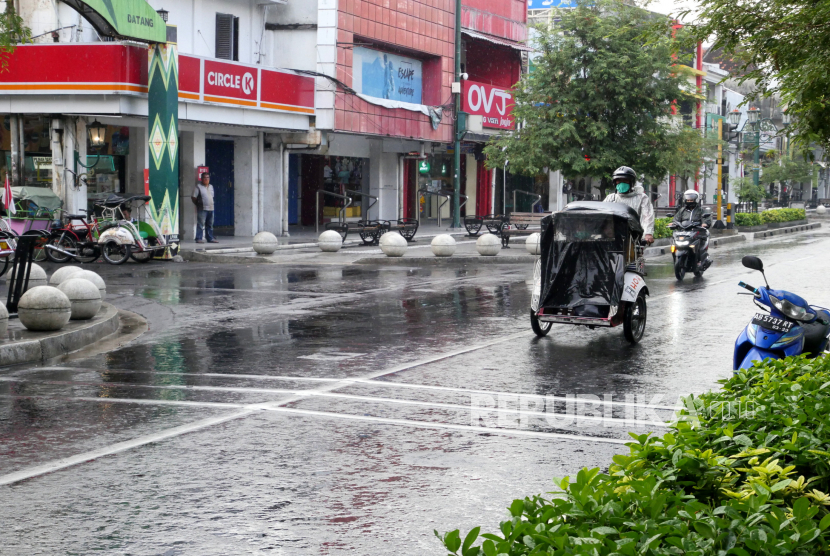 Pengendara becak bermotor menggunakan jas hujan melintas di kawasan Malioboro, Yogyakarta.