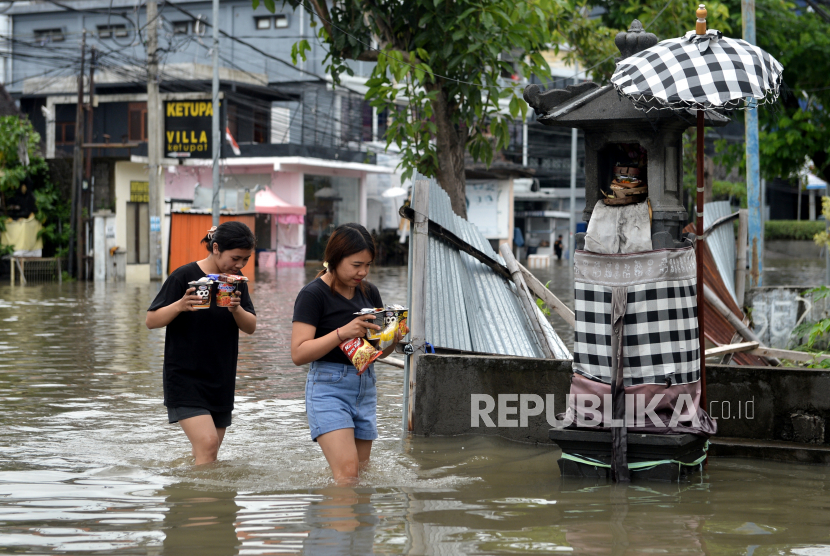 Warga berjalan menerobos banjir yang menggenangi kawasan Legian, Kuta, Badung, Bali, Senin (6/12). Hujan deras yang mengguyur wilayah Bali sejak Minggu (5/12) mengakibatkan banjir di sejumlah titik di kawasan Kuta dengan ketinggian air yang bervariasi. 