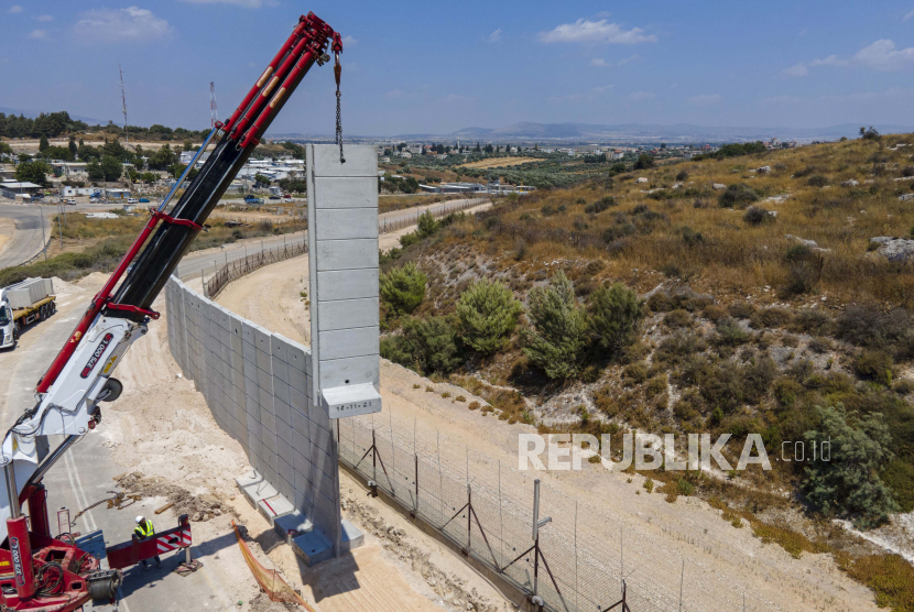 Para pekerja memasang tembok beton setinggi sembilan meter (30 kaki) yang menggantikan pagar perbatasan antara Tepi Barat utara dan Israel di dekat desa Arab Salem, Rabu (22/6/2022). Israel mulai melaksanakan pembangunan tembok beton dekat Jalur Gaza.