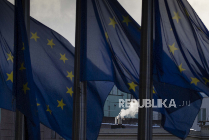  Asap mengepul dari cerobong asap di belakang bendera Uni Eropa yang berkibar tertiup angin di luar markas Uni Eropa di Brussel. Uni Eropa setuju untuk mendukung bantuan keuangan kepada Ukraina. Ilustrasi.