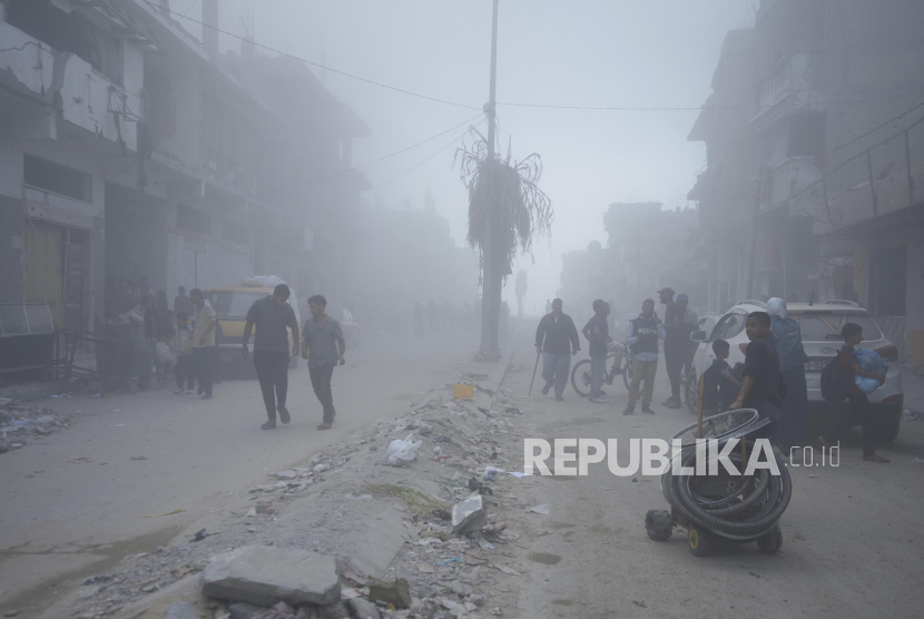 Warga Palestina berjalan melintasi puing-puing rumah yang hancur akibat serangan Israel di Khan Younis, Jalur Gaza.