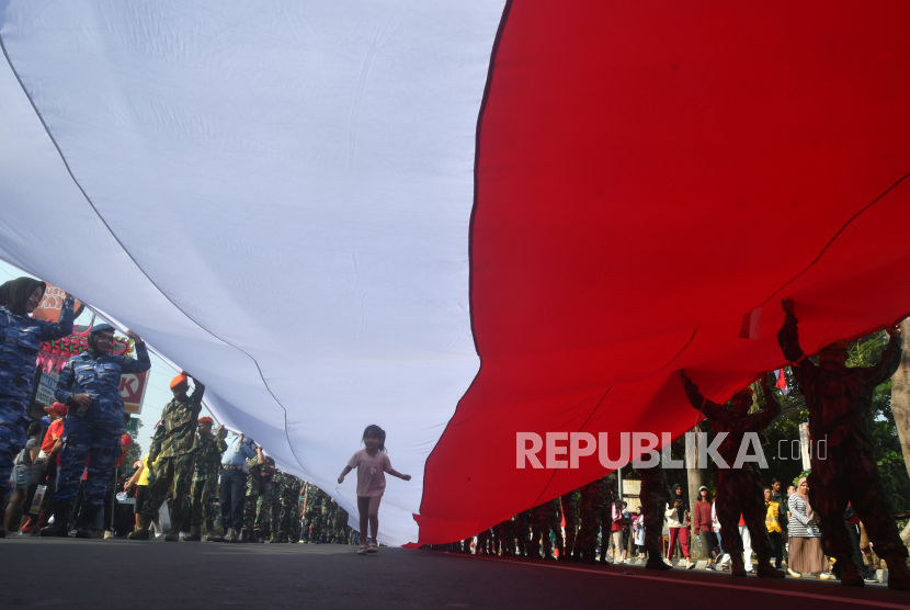 Seorang anak berlari di bawah bendera saat Kirab Merah Putih di jalan Sudirman, Kota Bogor, Jawa Barat, Ahad (18/8/2024). Kirab yang mengarak Bendera Merah Putih dengan panjang 200 meter dan lebar enam meter, sejauh empat kilometer tersebut merupakan rangkaian kegiatan Festival Merah Putih 2024 dalam rangka memperingati HUT ke-79 Kemerdekaan Republik Indonesia. 