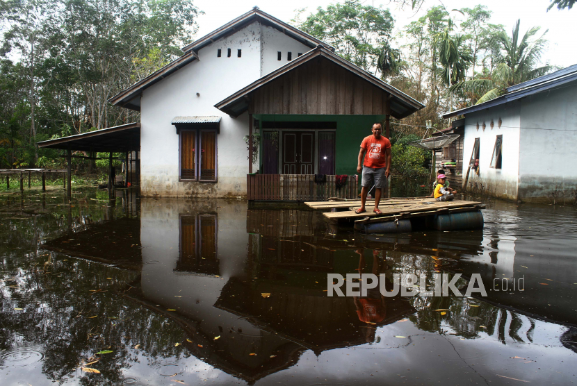 Seorang warga bersama anaknya menaiki rakit saat melintasi pemukiman yang terendam banjir (ilustrasi).