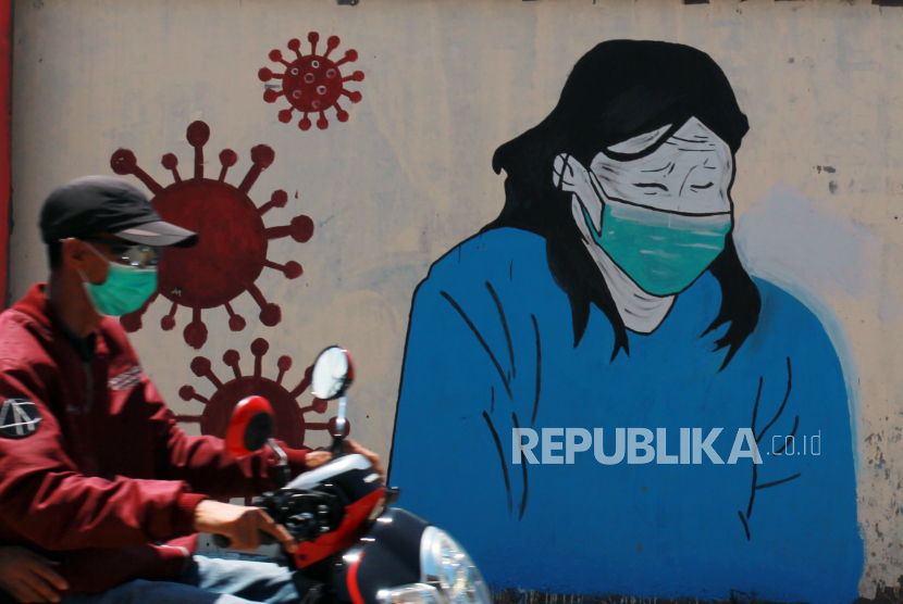 Pengendara motor melintas di depan mural tentang pandemi virus corona atau COVID-19 yang ada di Selapajang, Tangerang, Banten, Selasa (31/3/2020). Mural yang dibuat oleh warga setempat ditujukan sebagai bentuk keprihatinan atas merebaknya virus corona atau COVID-19 di Indonesia