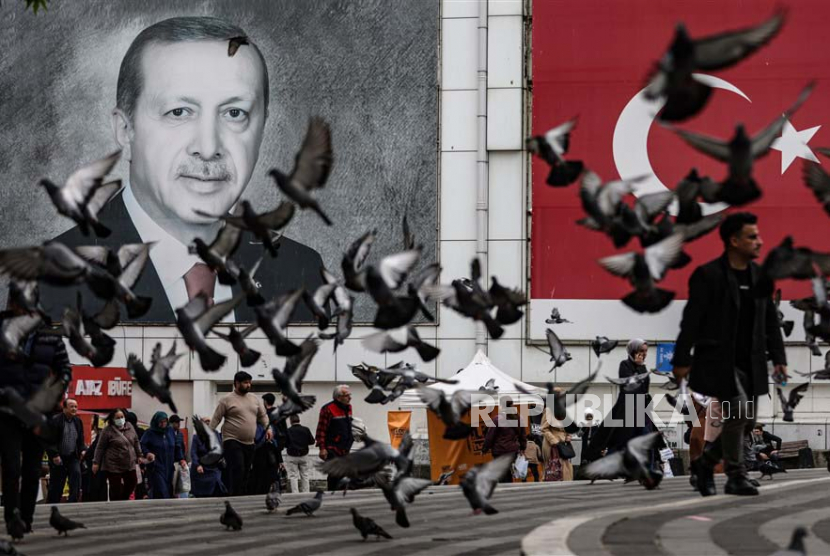 Orang-orang melewati potret Presiden Turki Recep Tayyip Erdogan dan bendera Turki di Bursa, Turki, Kamis (11/5/2023). Turki akan mengadakan pemilihan umum pada 14 Mei 2023 dengan sistem dua putaran untuk memilih presidennya, sedangkan pemilihan parlemen akan diadakan secara serentak .