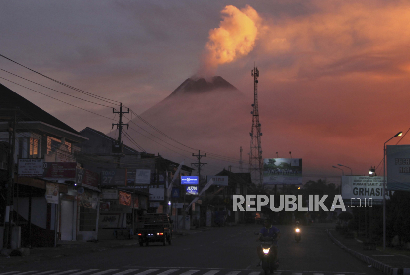Pengendara melintas saat Gunung Merapi tampak di latar belakang, di Sleman, Jumat, 25 Juni 2021. Gunung berapi paling volatil di Indonesia meletus pada hari Jumat, melepaskan gumpalan abu tinggi ke udara dan mengirimkan aliran lava dengan awan gas membakar yang mengalir di lerengnya.