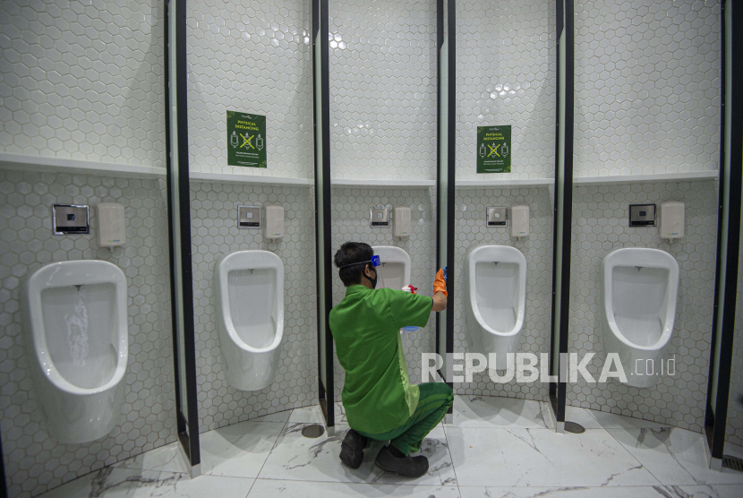 Petugas membersihkan fasilitas toilet dengan berstiker tanda jaga jarak .