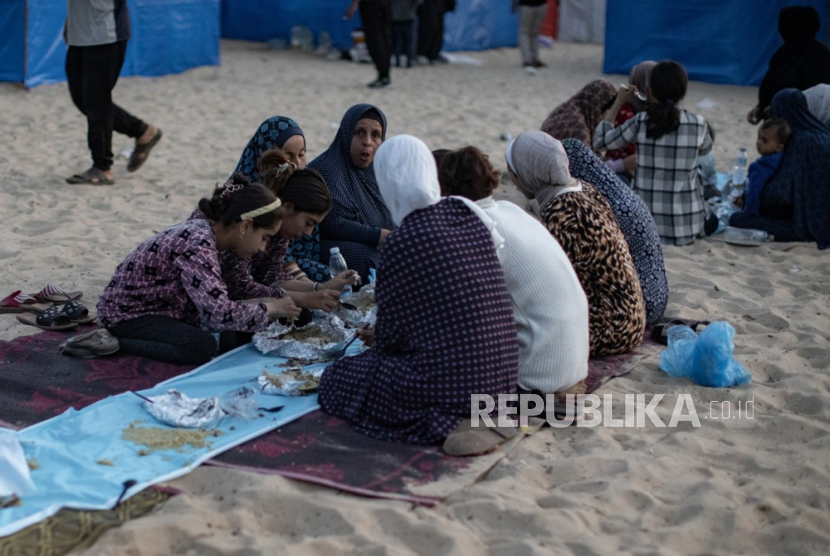 Pengungsi duduk bersama di samping tenda mereka untuk makan selama bulan suci Ramadhan pada acara buka puasa bersama yang diselenggarakan oleh kelompok sukarelawan pemuda di kamp Rafah di selatan Jalur Gaza, Rabu (27/3/2024).