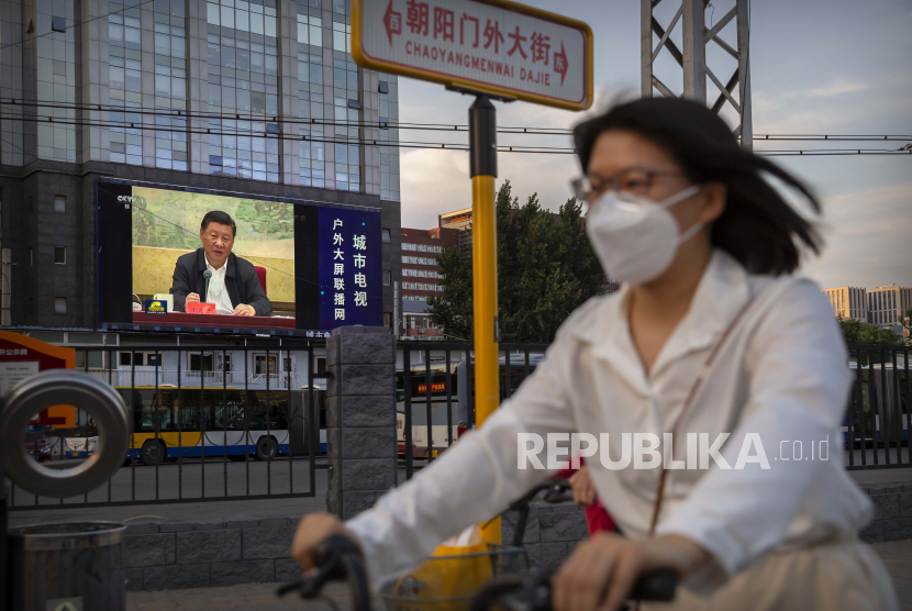 Seorang wanita mengenakan masker untuk melindungi terhadap virus corona baru naik sepeda melewati layar video besar 