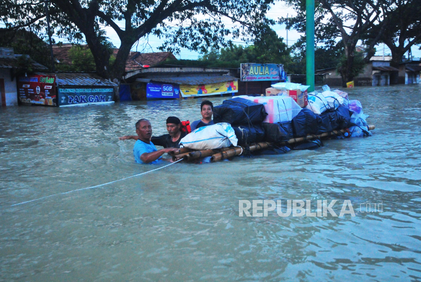 Warga korban banjir mengangkut bahan pokok menggunakan rakit melintasi jalan pantura yang terendam banjir di Karanganyar, Kabupaten Demak, Jawa Tengah, Senin (12/2/2024). 
