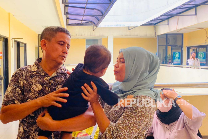 Pasangan suami istri Tabrani dan Siti Mauliah, menggendong anak kandungnya yakni GB (1) yang sempat tertukar di RS Sentosa Bogor tahun lalu. Saat ini dua keluarga bayi tertukar tengah menjalani proses bonding di Unit PPA Polres Bogor, Senin (4/9/2023). 