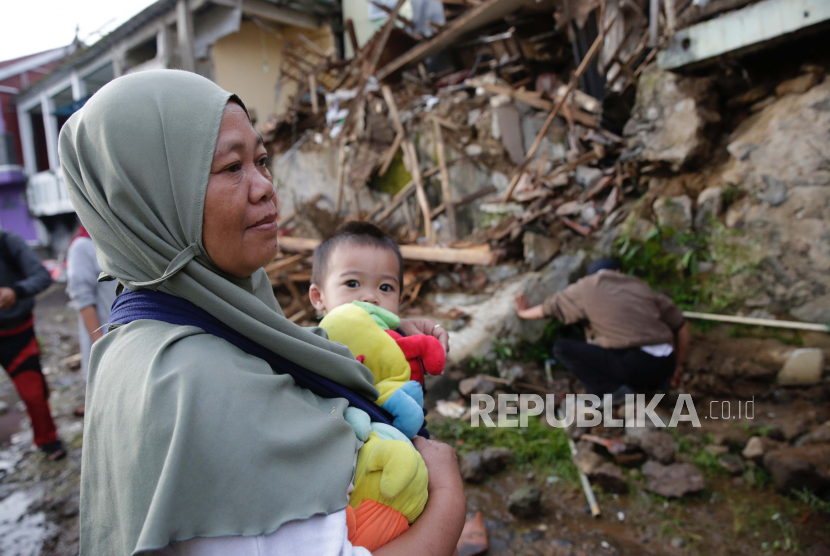 Seorang ibu menggendong anaknya di depan rumahnya yang rusak akibat gempa di Cianjur.