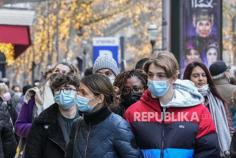  Pembeli yang mengenakan masker wajah untuk melindungi diri dari COVID-19 berjalan di sepanjang Grand Bouvard di Paris, Senin, 20 Desember 2021. Menurut WHO, Covid-19 belum bisa diperlakukan seperti penyakit flu biasa. 
