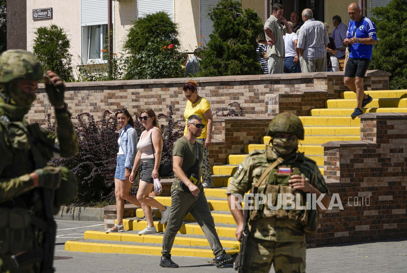 Orang-orang berjalan melewati saat tentara Rusia menjaga kantor untuk aplikasi kewarganegaraan Rusia, di Melitopol, Ukraina selatan, 14 Juli 2022. Foto ini diambil selama perjalanan yang diselenggarakan oleh Kementerian Pertahanan Rusia.
