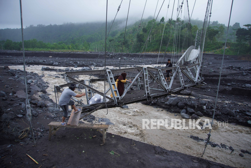 Warga melintas di Jembatan Gantung Kaliregoyo di Dusun Sumberwuluh, Candipuro, Lumajang, Jawa Timur. Jembatan penghubung Desa Jugosari dengan Sumberwuluh ini putus akibat banjir lahar hujan . 