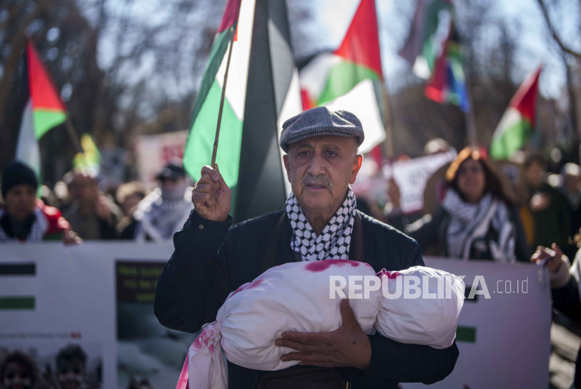 Seorang pria memegang boneka untuk melambangkan bayi. saat protes mendukung Palestina dan menyerukan gencatan senjata segera di Gaza, di Madrid, Spanyol, Sabtu, (20/1/2024).