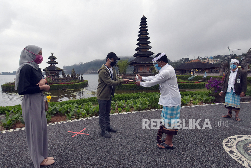 Petugas dengan alat pelindung dan masker di wajahnya memberikan cairan hand sanitizer kepada wisatawan saat pembukaan obyek wisata Ulun Danu Beratan, Tabanan, Bali. Kemenparekraf menyatakan revitalisasi wisata Bali akan dilanjutkan.