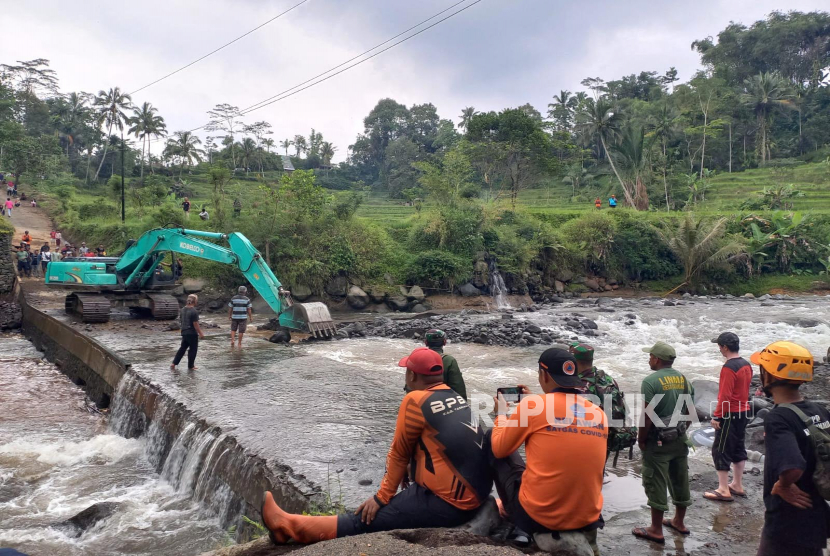 Petugas dan warga melihat alat berat yang membersihkan sumbatan cekdam di bawah Jembatan Cidugaleun, Kecamatan Cigalontang, Kabupaten Tasikmalaya, Senin (8/5/2023). Cekdam itu akan digunakan untuk jalur alternatif sementara karena oprit Jembatan Cidugaleun ambruk pada Ahad (7/5/2023) sore. 