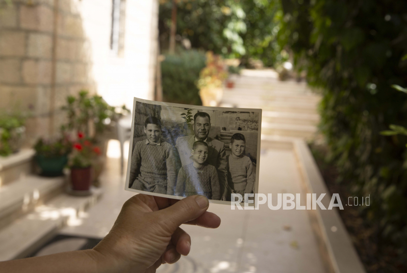 Warga Sheikh Jarrah Diminta Akui Tanah Milik Israel. Samira Dajani memegang foto ayahnya, Fouad Moussa Dajani dan putra-putranya, diambil di tempat yang sama di halaman rumah mereka di lingkungan Sheikh Jarrah di Yerusalem timur, Minggu, 9 Mei 2021. Ketika keluarga Samira Dajani pindah ke rumah mereka Rumah sungguhan pertama pada tahun 1956 setelah bertahun-tahun sebagai pengungsi, ayahnya menanam pohon di taman, menamainya untuk masing-masing dari enam anaknya.