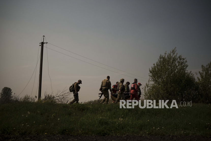 Prajurit Ukraina dan pekerja darurat membawa mayat seorang tersangka tentara Rusia di Malaya Rohan, sebuah desa yang direbut kembali oleh pasukan Ukraina di pinggiran Kharkiv, Ukraina, Ahad, 8 Mei 2022.