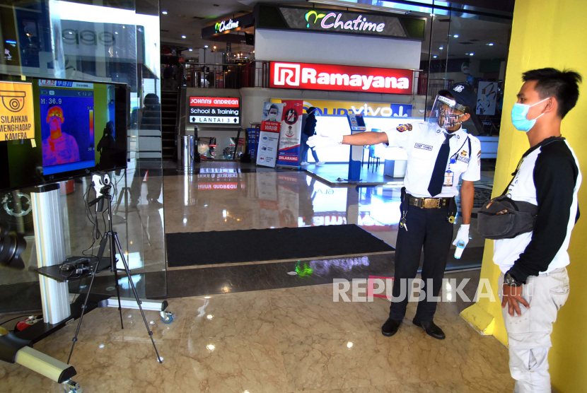 Petugas keamanan memeriksa suhu tubuh pengunjung melalui layar saat pembukaan kembali pusat perbelanjaan. Ilustrasi