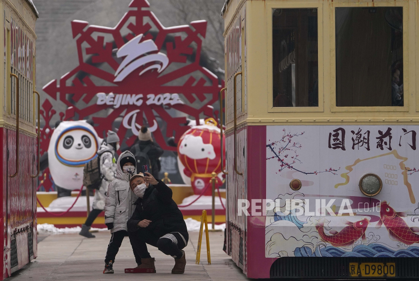  Seorang pria dan seorang anak mengenakan masker untuk membantu melindungi dari virus corona mengambil selfie dengan dekorasi untuk Olimpiade Musim Dingin Beijing di antara kereta yang diparkir di Qianmen Street, tempat wisata populer di Beijing, Ahad, 23 Januari 2022 