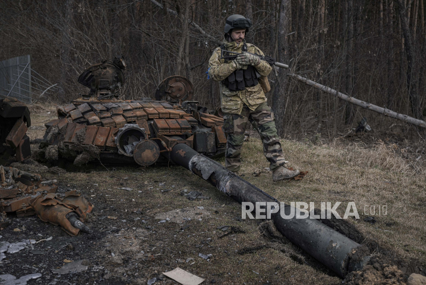 Seorang prajurit Ukraina berjalan di samping bangkai tank Rusia di Stoyanka, Ukraina, Ahad, 27 Maret 2022. Beberapa prajurit Rusia mencari bantuan hukum untuk menghindari tugas perang ke Ukraina. 