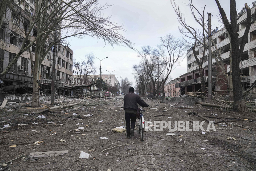 Seorang pria berjalan dengan sepeda di jalan yang rusak akibat penembakan di Mariupol, Ukraina, 10 Maret 2022.