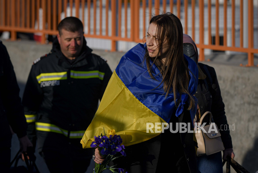 Seorang pengungsi yang melarikan diri dari perang dari negara tetangga Ukraina berjalan dengan bendera Ukraina tersampir di bahunya, setelah melintasi perbatasan dengan feri di penyeberangan perbatasan Isaccea-Orlivka di Rumania, Rabu (23/3/2022).