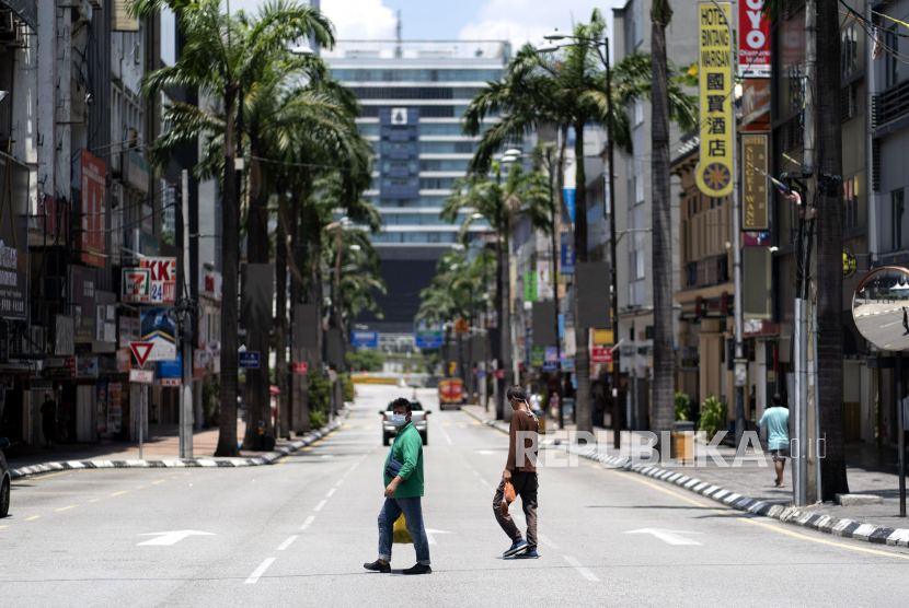 Pejalan kaki yang memakai masker menyeberang jalan kosong di pusat kota Kuala Lumpur, Malaysia, Ahad (12/4). Malaysia memperpanjang penguncian wilayah atau lockdown selama dua pekan hingga 28 April 2020 untuk menekan penyebaran virus corona