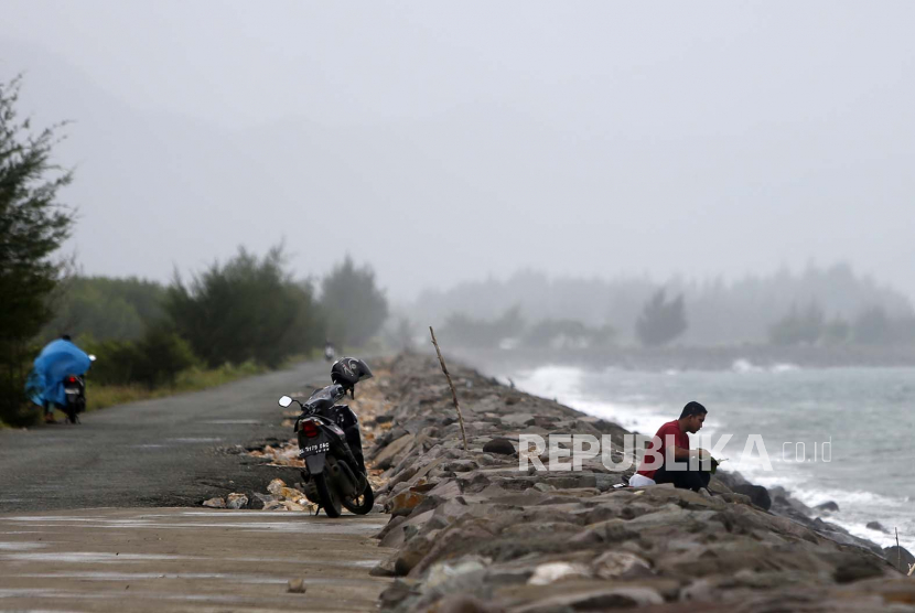 Pria duduk di pantai saat gelombang besar dan hujan deras di Banda Aceh, Indonesia, 18 Oktober 2022. Badan Meteorologi dan Geofisika Aceh mengeluarkan peringatan tentang perubahan cuaca ekstrem di wilayah Aceh akibat pembelokan angin yang menyebabkan hujan lebat dengan potensi hujan banjir dan tanah longsor.