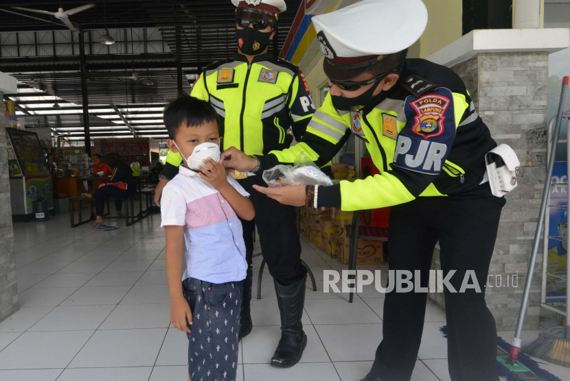 Petugas Kepolisian memakaikan masker kepada seorang anak di lingkungan rest area 234 Mesuji, Lampung, Selasa (25/8/2020). Dalam imbauannya petugas meminta para pengendara dan penumpang agar tetap melakukan protokol kesehatan pencegahan COVID-19 terutama pengunaan masker sebagai upaya untuk memutus rantai penyebaran COVID-19. 