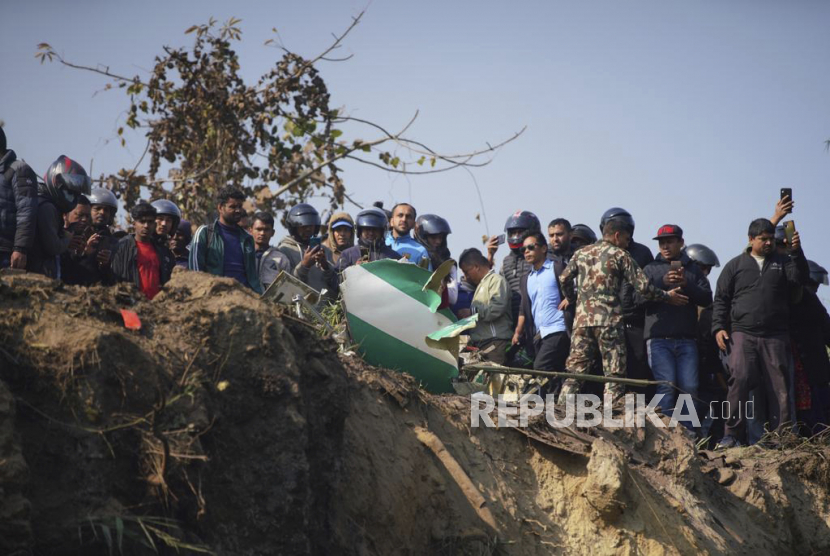 Warga menyaksikan reruntuhan pesawat penumpang di Pokhara, Nepal, Ahad, 15 Januari 2023. Sebuah pesawat penumpang dengan 72 orang di dalamnya jatuh di dekat Bandara Internasional Pokhara di Nepal, lapor surat kabar harian Kathmandu Post. Pesawat itu membawa 68 penumpang dan empat awak.