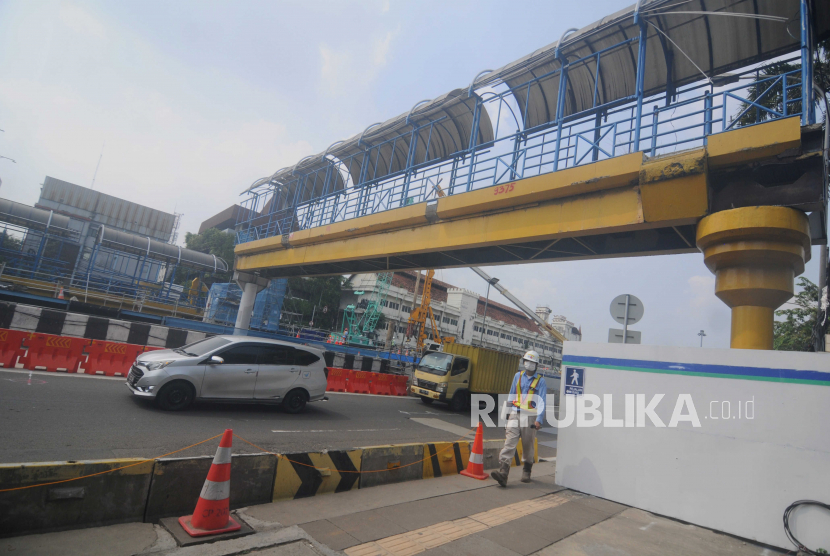 Petugas berjalan di dekat konstruksi jembatan penyeberangan orang (JPO) yang sedang dalam tahap pembongkaran di Jalan Gajah Mada, Jakarta Pusat, Jumat (26/5/2023).