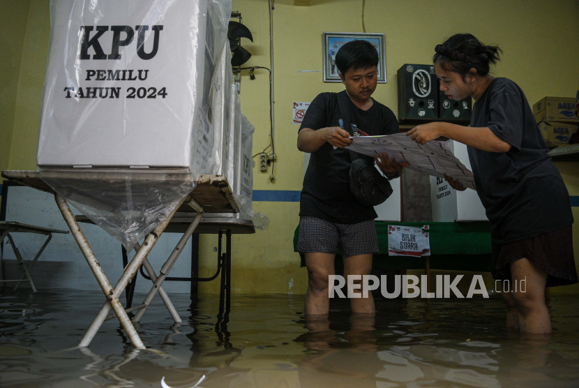 Dua petugas memeriksa surat suara di Tempat Pemungutan Suara (TPS) 039 yang terendam banjir di Duri Kepa, Kebon Jeruk, Jakarta, Rabu (14/2/2024). Banjir setinggi 50 centimeter akibat intensitas hujan tinggi dan luapan Kali Sekretaris tersebut menyebabkan pelaksanaan pencoblosan sempat tertunda di TPS 039 dengan 271 Daftar Pemilih Tetap (DPT) dan TPS 038 dengan 268 DPT. 