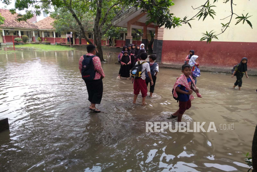 Sejumlah anak sekolah berjalan melewati banjir yang menggenangi halaman sekolah mereka (ilustrasi) 