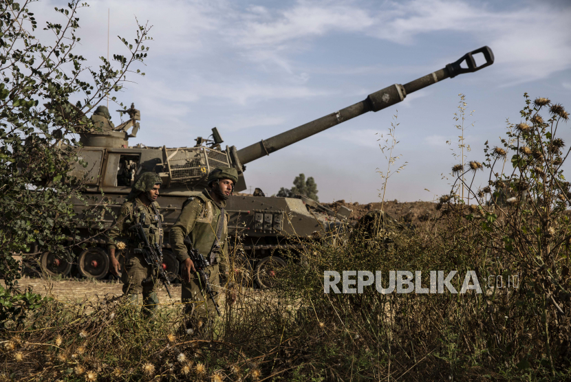 Dua tentara Israel berjalan di sekitar unit artileri, di perbatasan Gaza Israel, Minggu, 16 Mei 2021.