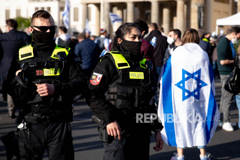 Wanita dengan bendera Israel di samping petugas polisi menghadiri rapat umum yang disebut solidaritas dengan Israel dan menentang antisemitisme di depan Gerbang Brandenburg di Berlin, Jerman, 20 Mei 2021.