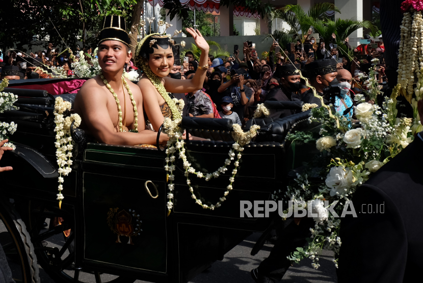 Putra bungsu Presiden Joko Widodo Kaesang Pangarep (kiri) didampingi istrinya Erina Gudono (kanan) menyapa warga saat mengikuti prosesi kirab budaya pada acara Ngunduh Mantu pernikahan di Jalan Slamet Riyadi Solo, Jawa Tengah, Minggu (11/12/2022). Acara tersebut juga diisi pesta rakyat. 