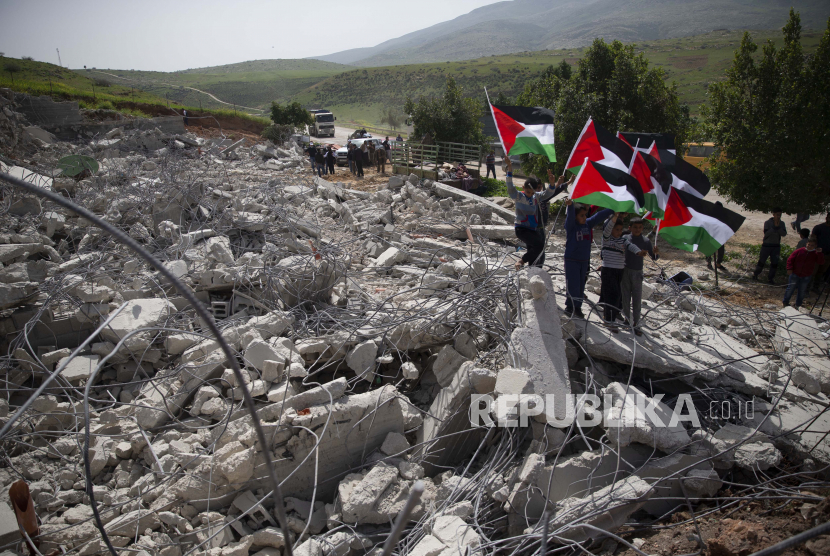  Pemuda Palestina membawa bendera nasionalnya di atas puing-puing rumah Palestina yang dibongkar pasukan Israel karena dibangun tanpa izin, di desa Ain Shibli di Lembah Jordan Tepi Barat, Rabu, Maret. 10, 2021.