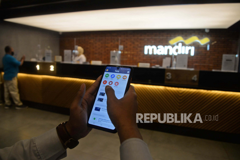 Nasabah dengan menggunakan ponsel melakukan transaksi menggunakan aplikasi mobile banking Livin Bank Mandiri di Kantor Cabang Mal Senayan City, Jakarta, Selasa (7/9). Pola transaksi nasabah selama masa pandemi secara tidak langsung mulai bergeser dari transaksi tunai ke digital. Tercatat hingga Juni 2021 jumlah pengguna Livin by Mandiri yang terdaftar telah mencapai 7,8 juta user dengan nilai transaksi mencapai Rp 728,9 triliun atau tumbuh 59% secara year on year (YoY).Prayogi/Republika.