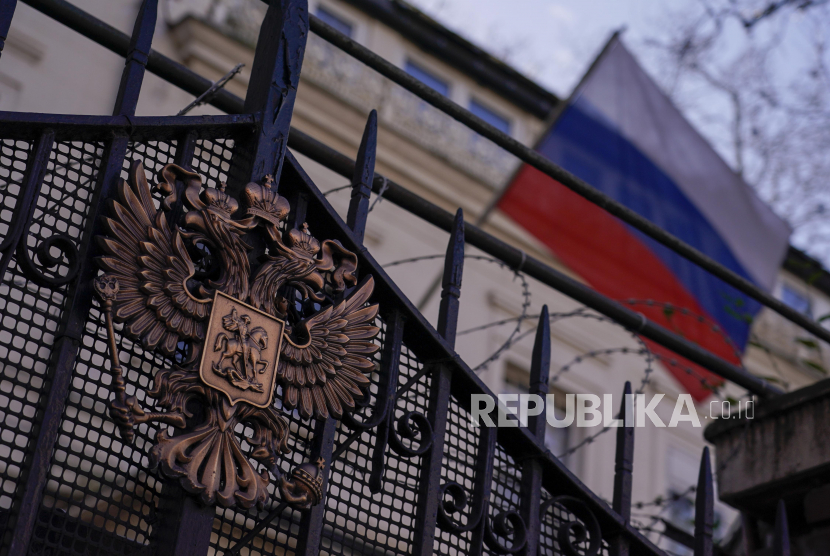 Lambang Rusia terlihat di gerbang kedutaan saat bendera nasional melambai di latar belakang, di London, Jumat, 25 Februari 2022. Rusia berencana menyita aset perusahaan asing.