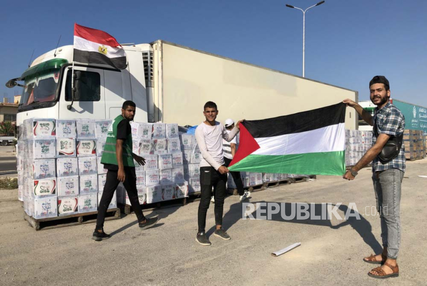 Dua pria menunjukkan bendera Palestina di depan truk konvoi bantuan kemanusiaan untuk Jalur Gaza.