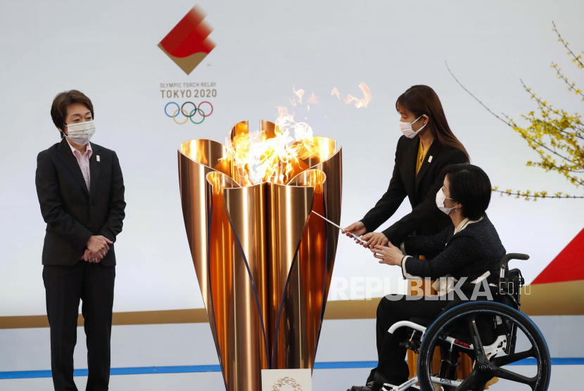 Presiden Tokyo 2020 Seiko Hashimoto, kiri, menyaksikan aktris Jepang Satomi Ishihara dan Paralympian Aki Taguchi menyalakan kuali perayaan pada hari pertama estafet obor Olimpiade Tokyo 2020 di Naraha, prefektur Fukushima, timur laut Jepang, Kamis (25/3).