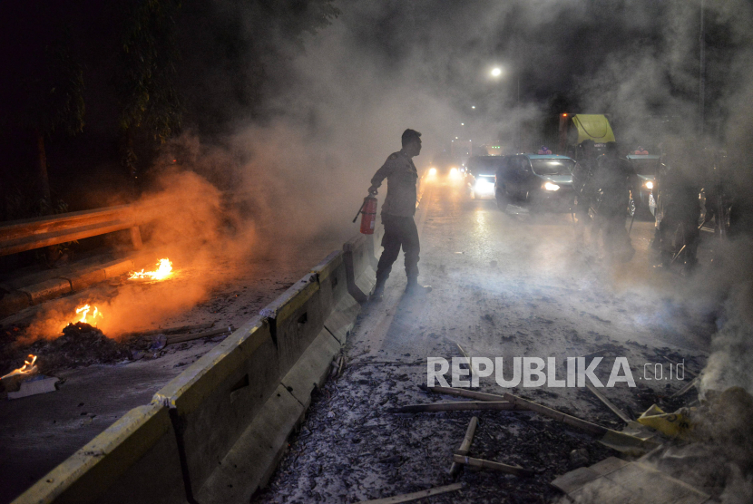 Petugas kepolisian berusaha memadamkan api dari bambu dan plastik yang dibakar massa aksi menolak pengesahan Revisi UU Pilkada di Fly Over Slipi Petamburan, Jakarta, Kamis (22/8/2024).  Aksi pembakaran bambu dan plastik serta upaya menutup jalan raya ini menimbulkan tersendatnya arus lalu lintas di kawasan tersebut.