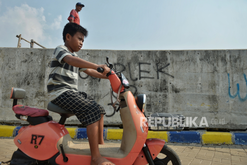 Warga mengendarai sepeda listrik melintas di dekat tanggul pengaman pantai yang retak di kawasan pesisir Kalibaru, Cilincing, Jakarta, Kamis (9/5/2024). Tanggul yang berfungsi mengurangi dampak banjir rob dan rembesan air laut sekitar Cilincing itu mengalami keretakan sehingga dapat membahayakan warga yang beraktivitas di kawasan tersebut.