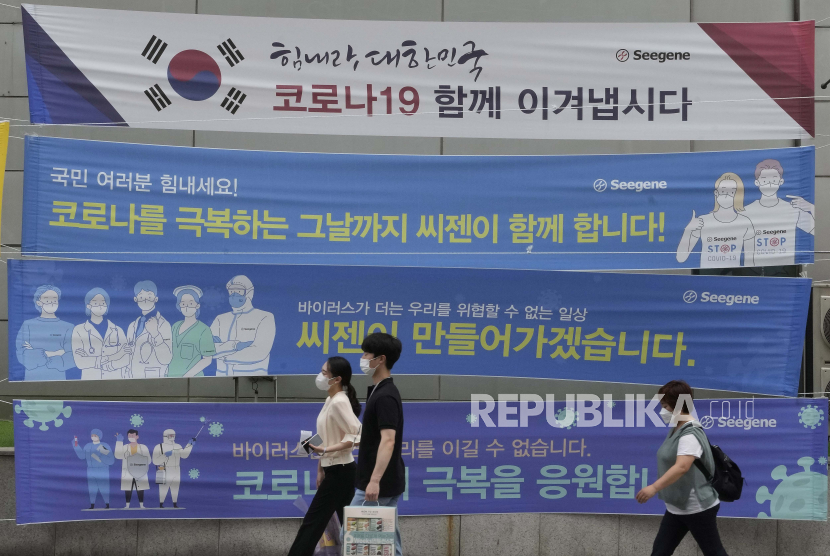 Orang-orang yang memakai masker melewati spanduk yang berharap untuk mengatasi krisis COVID-19 di sebuah jalan di Seoul, Korea Selatan, Selasa, 13 Juli 2021.