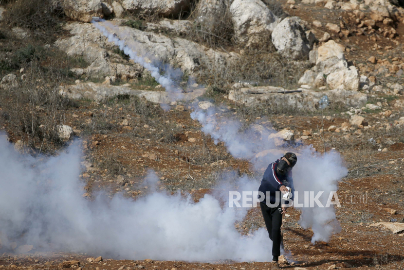 Pria Palestina melemparkan granat gas air mata ke pasukan Israel selama bentrokan yang meletus menyusul demonstrasi menentang permukiman Israel di Tepi Barat, 16 Desember 2022. 
