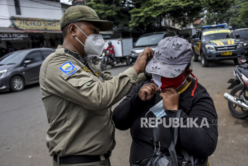 Petugas Satpol PP Kota Bandung membantu memasangkan masker ke warga saat operasi gabungan patroli pengawasan dan penegakan disiplin (Gakplin) protokol kesehatan Covid-19 di permukiman warga di Kelurahan Ciroyom, Kecamatan Andir, Kota Bandung, Selasa (16/2). Operasi yang digelar serentak di 30 kecamatan di Kota Bandung tersebut dalam rangka pemberlakuan pembatasan kegiatan masyarakat (PPKM) skala mikro guna menertibkan masyarakat agar lebih disiplin dalam menerapkan protokol kesehatan Covid-19 serta mencegah penyebaran Covid-19 di tingkat desa atau kelurahan. Foto: Abdan Syakura/Republika